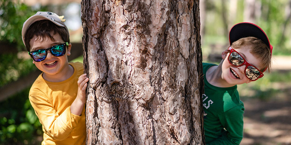 boys with sunglasses behind a large tree