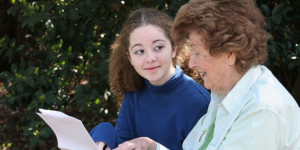 girl and elderly lady hold a sheet of paper together outdoors