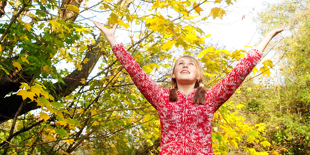 girl with arms outstretched beneath a tree