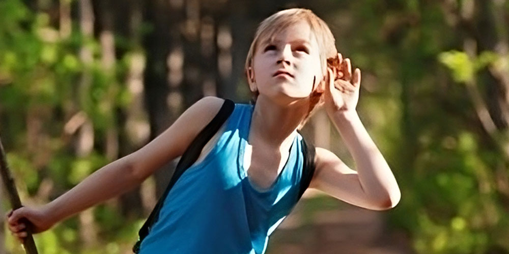 boy with hand to his ear listing to forest sounds