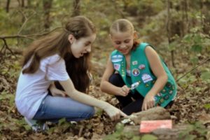 Girls point at and examine something on the ground in a forest