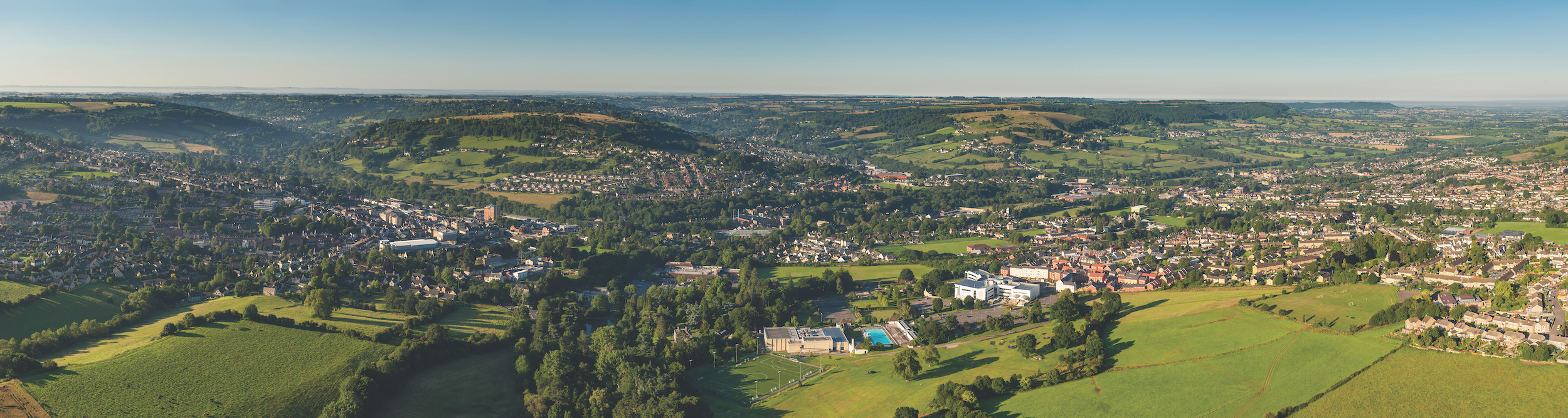 Aerial view over homes, streets and suburban community at the edge of picturesque country town surrounded by green pasture and farmland, Stroud, UK. ProPhoto RGB profile for maximum color fidelity and gamut.