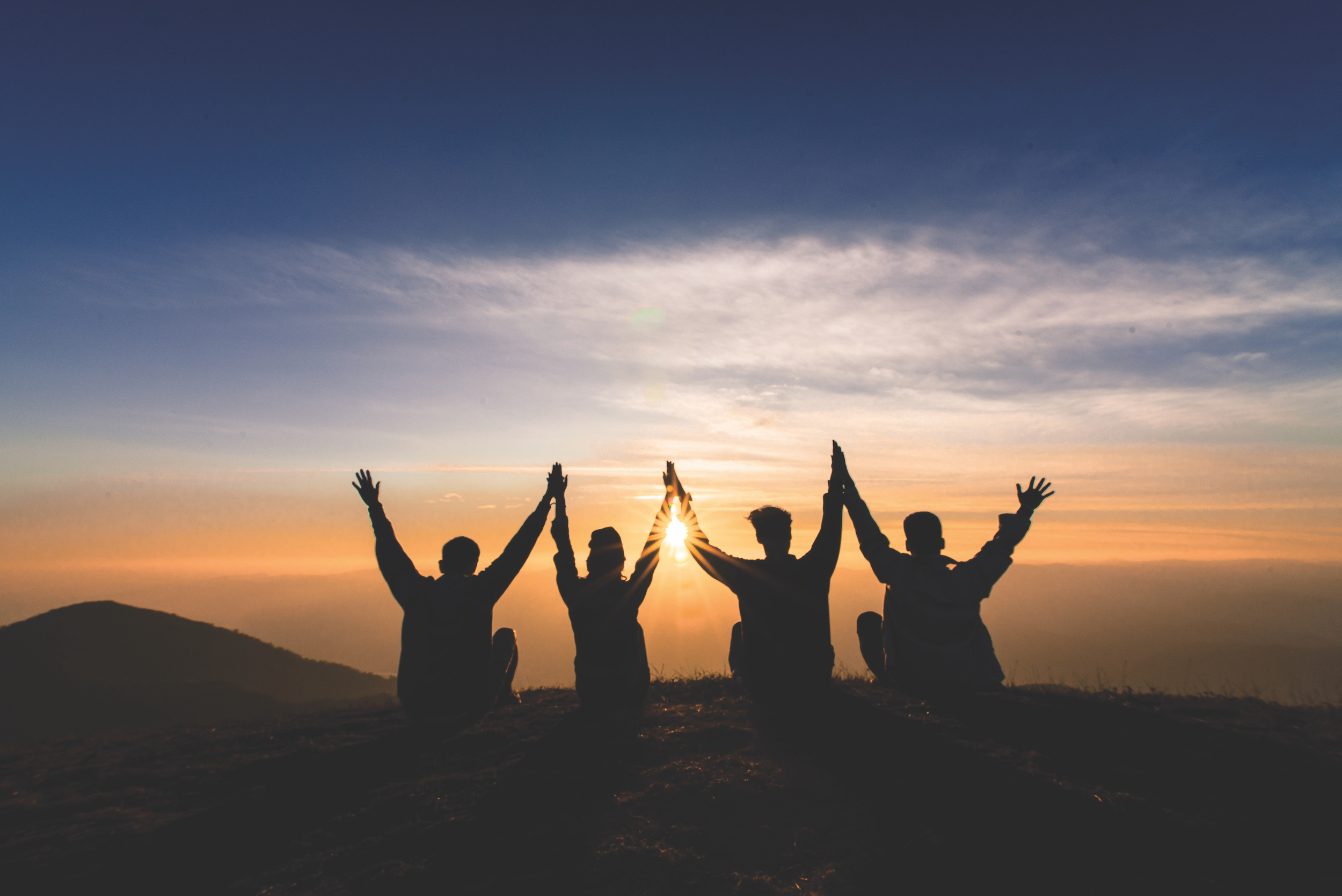 silhouette of friends shake hands up and sitting together in sunset for happiness,business successful and team work concept.