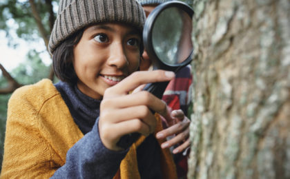 Young teen examining the tree stem through with magnifying glass.