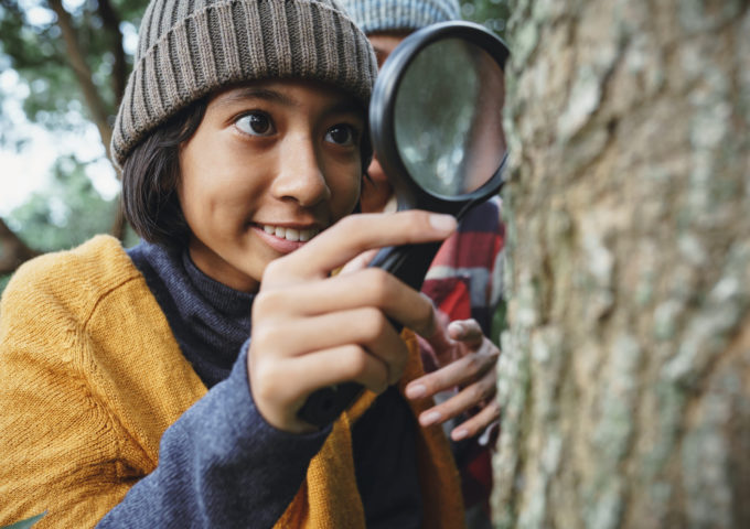 Young teen examining the tree stem through with magnifying glass.