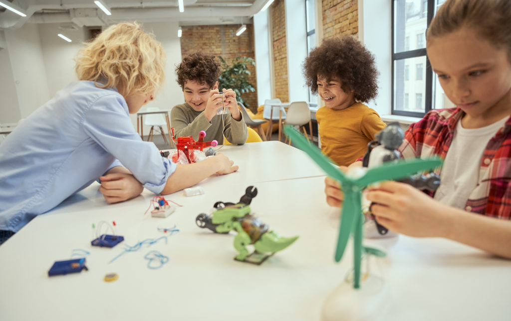 Children examining technical toys while sitting together at the table during STEM class. Engineering, afterschool activity.