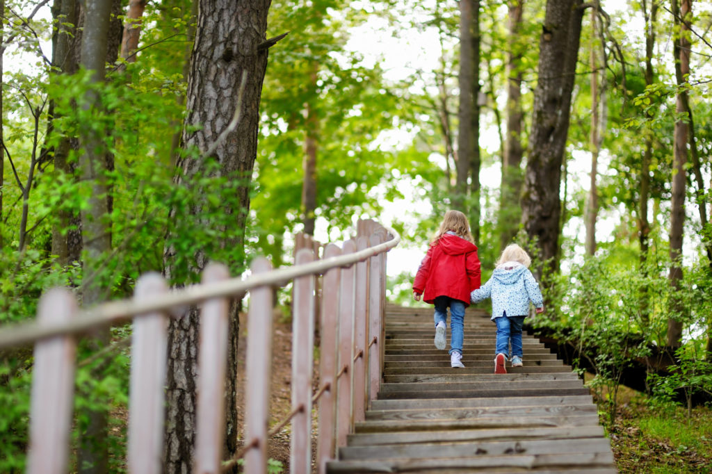 Two little sisters walking up stairs in summer park on beautiful sunny day