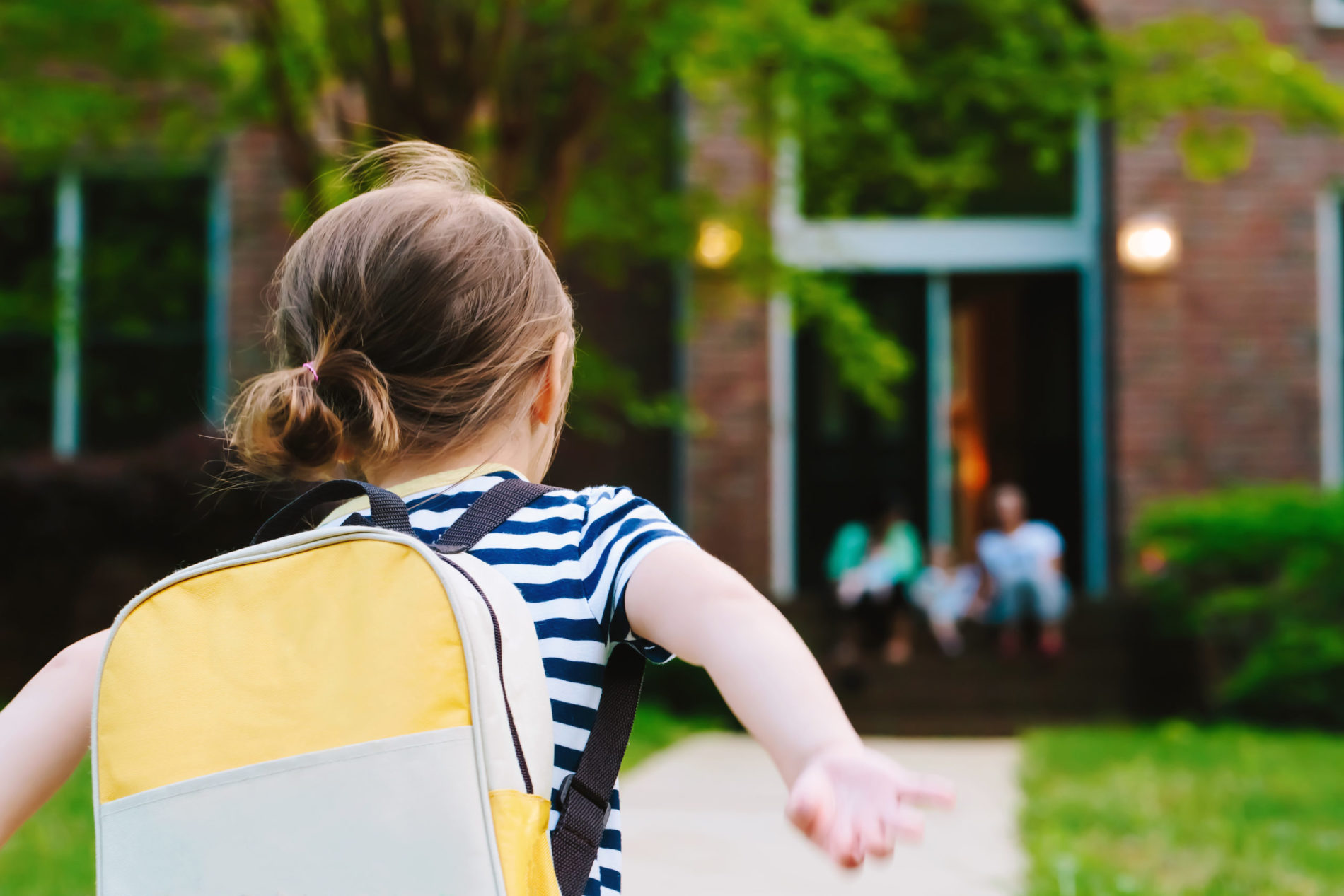 Young girl running towards school with a backpack