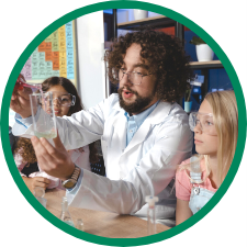 Latino teacher shows two young female students solution in a beaker