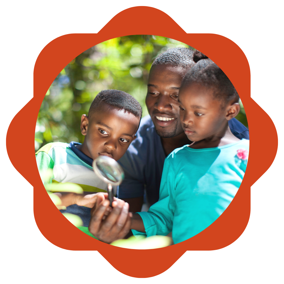 2 young kids and a fathering looking through a magnifying glass at a bush in the forest