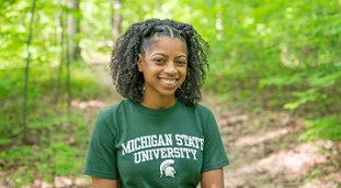 Woman in Michigan State University Tshirt stands in a forester