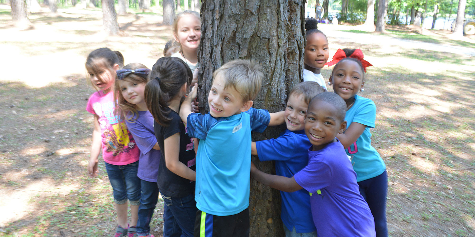 A group of kids with their arms around a big tree trunk