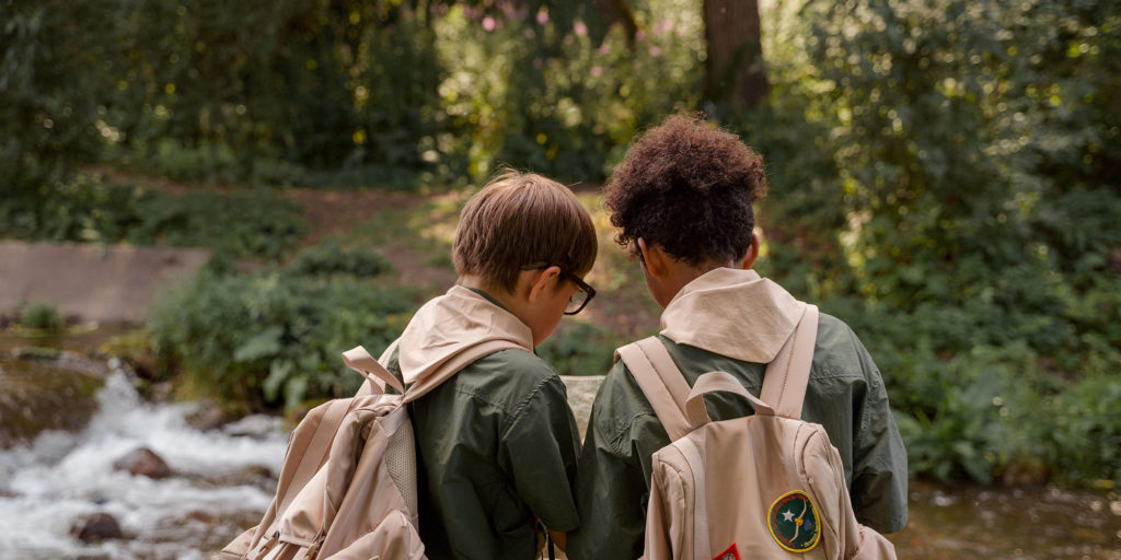 Two young boys in scouts uniforms look at a map together in the forest.