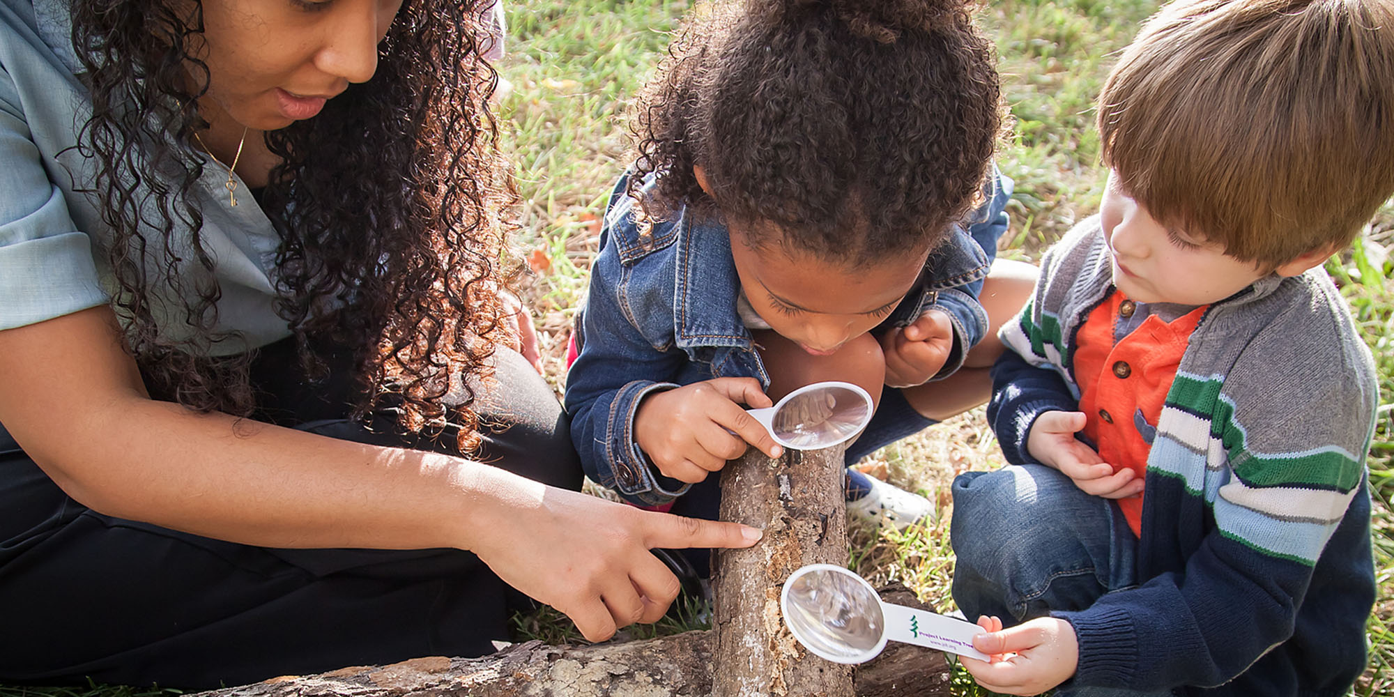 woman and children examining a tree branch with magnifying lenses
