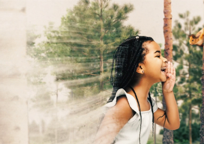 A young girl surrounded by trees calls out in play.