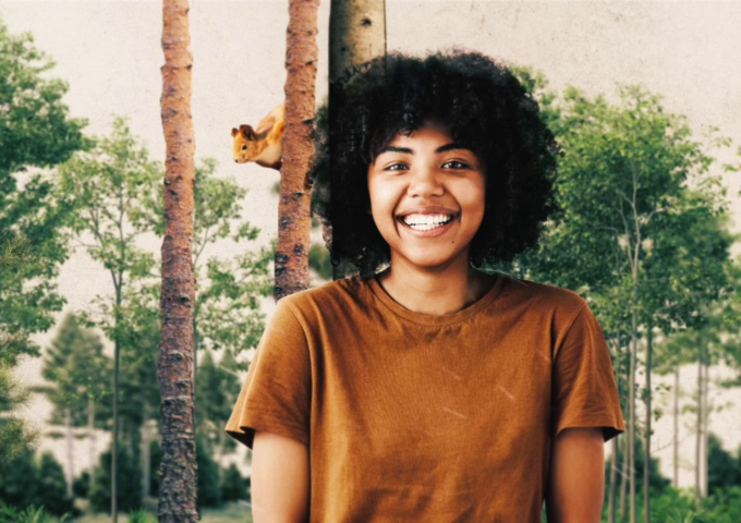 A young woman smiles in a grove of trees.