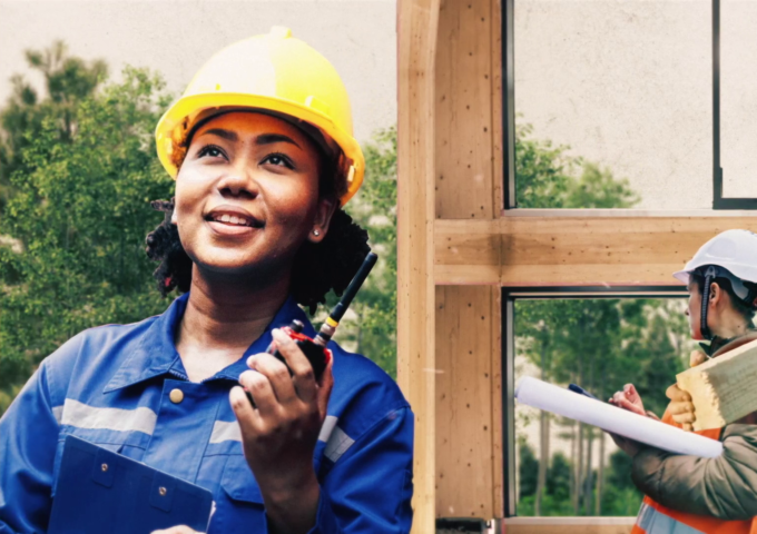 Woman in a hardhat holds a walkie talkie at a construction site.